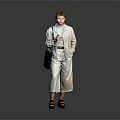 Woman In Light Gray Jumpsuit With Belt Holding Black Handbag Standing Against Dark Background