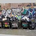 Public Trash Bins Against Graffiti Covered Brick Walls With Overflowing Trash And Art