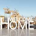 Welcome Home Letter Decorative Setup With Floral Arrangements And Brick Floor