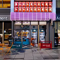 Stylish Storefront Featuring Purple Awning Red Sign White Icons Glass Doors and Outdoor Seating