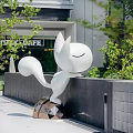 White Cat Sculpture Leaning On Black Scenic Wall With Green Plants Around