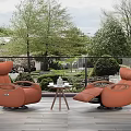 Two Orange Single Sofas on Outdoor Wooden Floor with Small Table and Trees