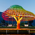 Vibrant Rainbow Colored Tree Sculpture With Circular Discs Near Lake And Mountains