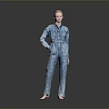 A Woman Standing Barefoot With Hands On Hips In Blue Denim Jumpsuit Against Gray Background