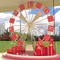 Decorative Ferris Wheel With Red Letters And Gift Boxes Against City Skyline And Green Grass