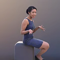 Woman In Blue Dress Sitting On Gray Object Smiling With Hands Gesturing