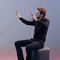 Man Sitting On Green Stool Raising Hands With Palms Out In Black Shirt And Blue Pants