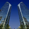 Modern Glass Office Towers Illuminated at Night With Blue Sky and Greenery at Base
