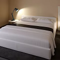 Modern Double Bed With White Striped Bedding Nightstand Lamp Beige Wall And Dark Rug