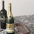 Green Champagne And Dark Wine Bottles On Marble Countertop With Brown Tray And Clear Cup