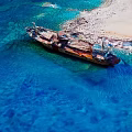 Rusty Shipwreck In Clear Blue Sea Near Shallow Water And Beach