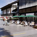 Vibrant Commercial Street With Outdoor Seating Green Umbrellas And Pedestrians Walking