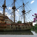 Ancient Sailing Ship In Waterfront Garden Landscape With Purple Flowers And Green Plants