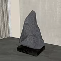 Gray Stone Sculpture On Black Wooden Base With Light Wall Curtain And Green Plant