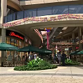 Outdoor Shopping Mall Area With Green Umbrellas Shops People And Decorative Arch