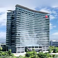 Modern High Rise Office Building With Glass Curtain Wall Red Logo And Surrounding Green Trees Blue Sky