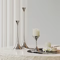 Silver Candle Holders Featuring White Lit Candle Small Candle and White Flowers on Light Tabletop