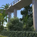 Commercial Landscape Featuring Concrete Viaduct Tall Columns Palm Trees Lush Bushes And Blue Sky