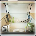 White Kitchen Cabinet Interior With Metal Racks Holding Dishes Cups And Green Bottles