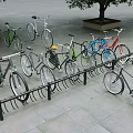 Colorful Bicycles Parked on Outdoor Bike Rack With Stone Pavement and Trees