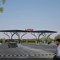 Charging Station Entrance Gate With LOGO And Vehicles Entering Under Blue Sky