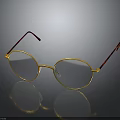 Round Eyeglasses With Gold Frame And Brown Temple Arms On Reflective Black Surface