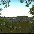 Tranquil Natural Landscape With Green Trees Flower Bushes And Distant City Under Blue Sky