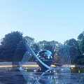 Modern Sculpture Featuring Metal Sphere And Curved Metal Strips In Water With Trees And Lighting