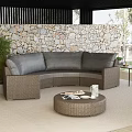 Outdoor Wicker Sofa With Gray Cushions Round Coffee Table And Green Plants By Stone Wall