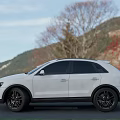 White Audi SUV Parked On Road With Mountains Trees And Red Flowers