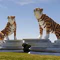 Two Tiger Statues Standing On Stone Pedestals In Grassy Field With Blue Sky