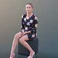 Young Woman In Floral Dress Sitting On Black Cylindrical Stool Against Dark Background