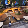Modern Commercial Street With Glass Buildings Billboards Outdoor Seating Vehicles And Pedestrians
