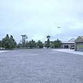 Industrial Factory With Open Space Surrounding Trees Gray Buildings Distant Tower Light Poles Overcast Sky