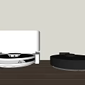 Black Smart Machine with Robotic Vacuum Cleaner on Wooden Tabletop against Light-colored Wall