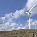 Public Wind Energy Facility with Multiple Turbines on Green Hillside Under Blue Sky and Clouds