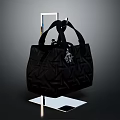 Black Quilted Handbag With Handles And Small Decorative Charm On Transparent Display Stand