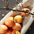 Ceramic Vessel Filled With Fresh Persimmons Surrounded By Dried Flowers And Glass With Ice
