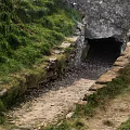 Stone Tunnel Entrance Surrounded by Lush Green Vegetation and Dirt Path