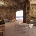 Cave Style Cafe With Stone Walls White Tables Chairs Bar And Sea View Through Window