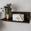 White fashion bag on dark wooden shelf with golden vase purple flowers and green plants