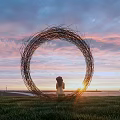 Round Woven Outdoor Chair Placed on Green Grass Field Facing Beautiful Sunset Sky