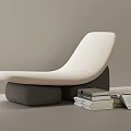 Modern White Curved Lounge Chair with Gray Base and Stacked Books in Interior
