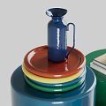 Vibrant Green Cup Beside Books With Blue Pitcher On Stacked Colorful Plates And Cylindrical Container