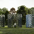 Three Metal Cubical Sculptures With Cylindrical Structure In Green Grassland With Trees