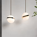Two Spherical White Pendant Lights With Gold Accents Against White Wall And Green Leaves