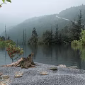 Misty Mountain Scenery With Calm Lake Reflection Lush Trees And Pebble Shore