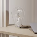 Modern Transparent Bulb Shaped Table Lamp On Wooden Desk With Laptop And Light Background