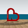 Red Heart Shaped Garden Ornament With LOVE LAND Text Overlooking Sea View On Wooden Platform