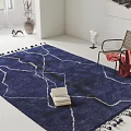 Blue Square Rug With White Patterned Lines And Tassels In Room With Chair And Books